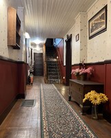 Un pasillo con alfombra estampada, suelo de madera, una escalera, un armario de madera con flores y un cuadro en la pared.