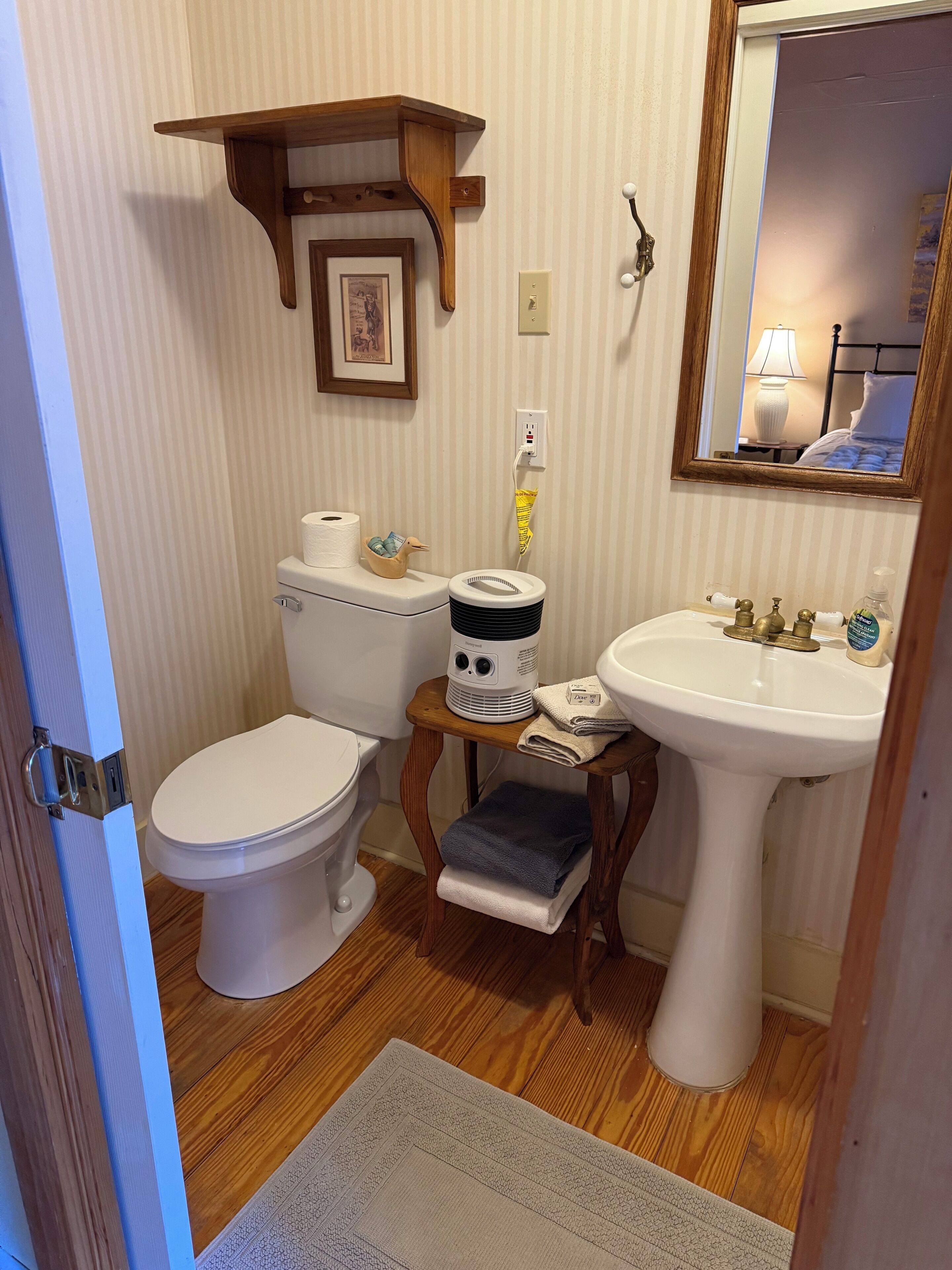 A bathroom with a toilet, sink, and a wooden shelf above the toilet.