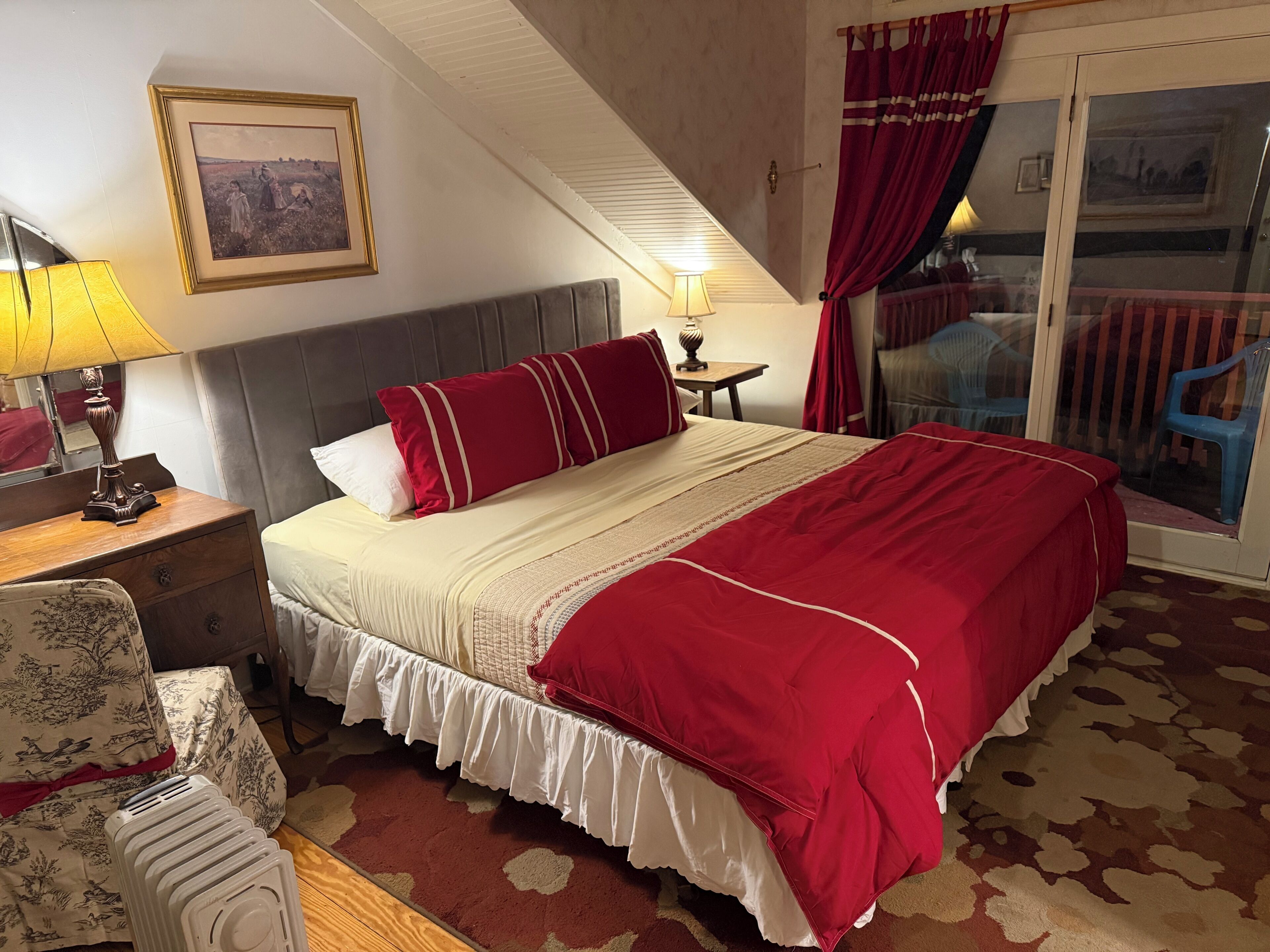 Una habitación de hotel con una cama grande, una mesita de noche con lámpara, una silla y una ventana con cortinas.