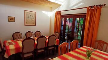 Un comedor con manteles a rayas, sillas de madera, una araña y vistas a través de una ventana con cortinas.