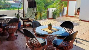 An outdoor patio with wicker furniture, a hanging chair, and a view of greenery and buildings. - The Cariari Bed and Breakfast (Ulloa)