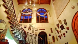 A staircase with ornate railings, a chandelier, and a view of the sky through arched windows. - The Cariari Bed and Breakfast (Ulloa)