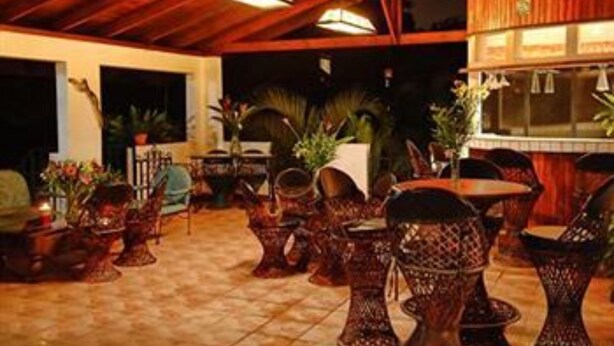 An indoor seating area with wicker chairs and tables, wooden beams on the ceiling, and potted plants. - The Cariari Bed and Breakfast (Ulloa)