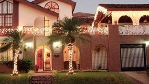 A two-story building with a red-tiled roof, arched windows, and a brick facade. There are palm trees and a well-maintained lawn in front. - The Cariari Bed and Breakfast (Ulloa)