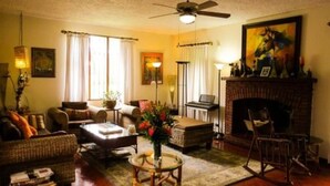 A cozy living room with a fireplace, comfortable seating, and a large window allowing natural light. - The Cariari Bed and Breakfast (Ulloa)
