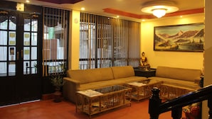 A living room with a sofa, two coffee tables, a Buddha statue, and a painting of mountains. - Hotel Buddha Land (Kathmandu)