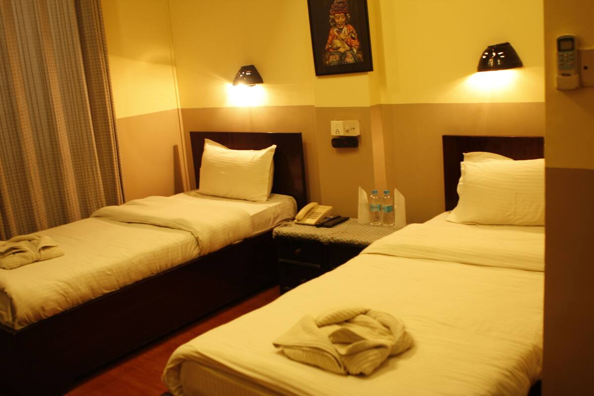 Two single beds with white linens, a telephone, and a small table with bottled water.
