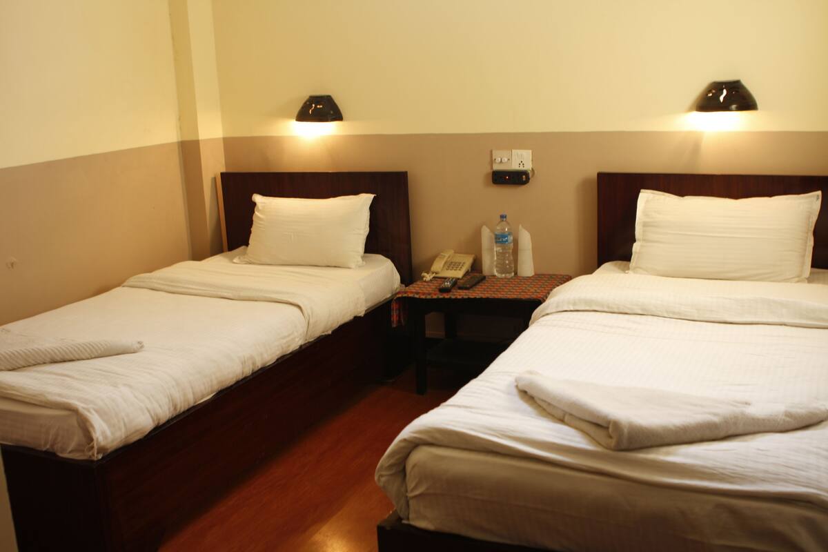 A hotel room with two single beds, a small table with a telephone and a water bottle, and a wall socket.