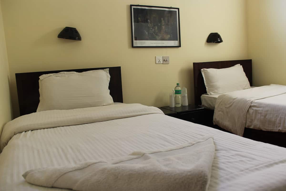 A hotel room with two beds, each with white linens, a framed picture on the wall, and two wall-mounted lamps.