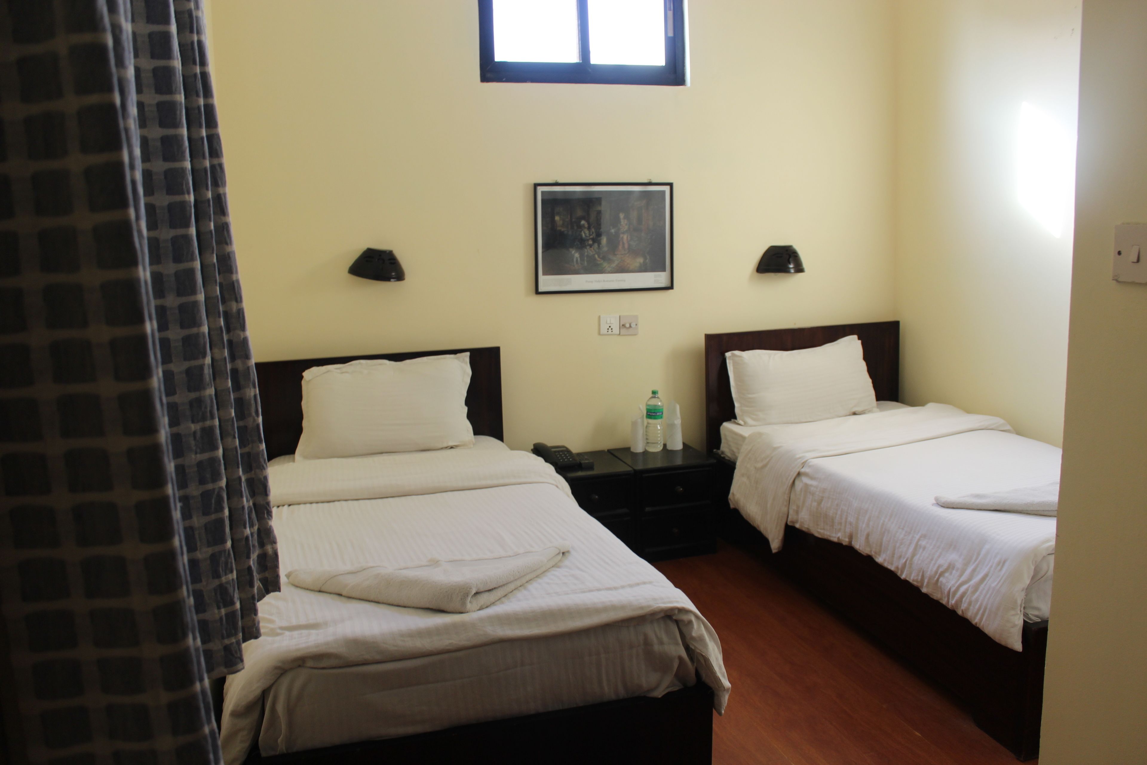 Camera d'albergo con due letti, un comodino, un quadro incorniciato appeso al muro e una finestra sopra i letti.