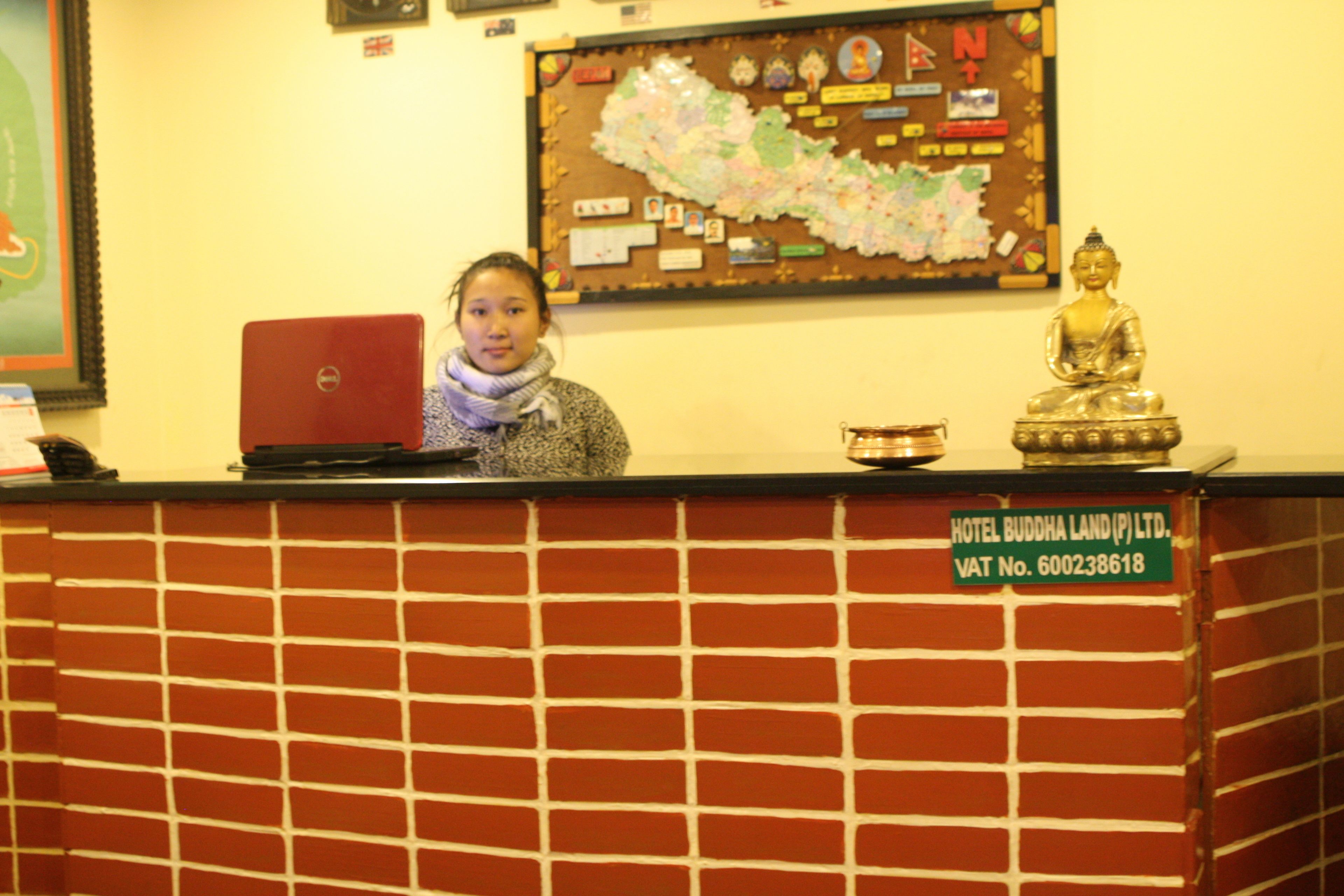 A reception desk with a laptop, a Buddha statue, and a wall map.