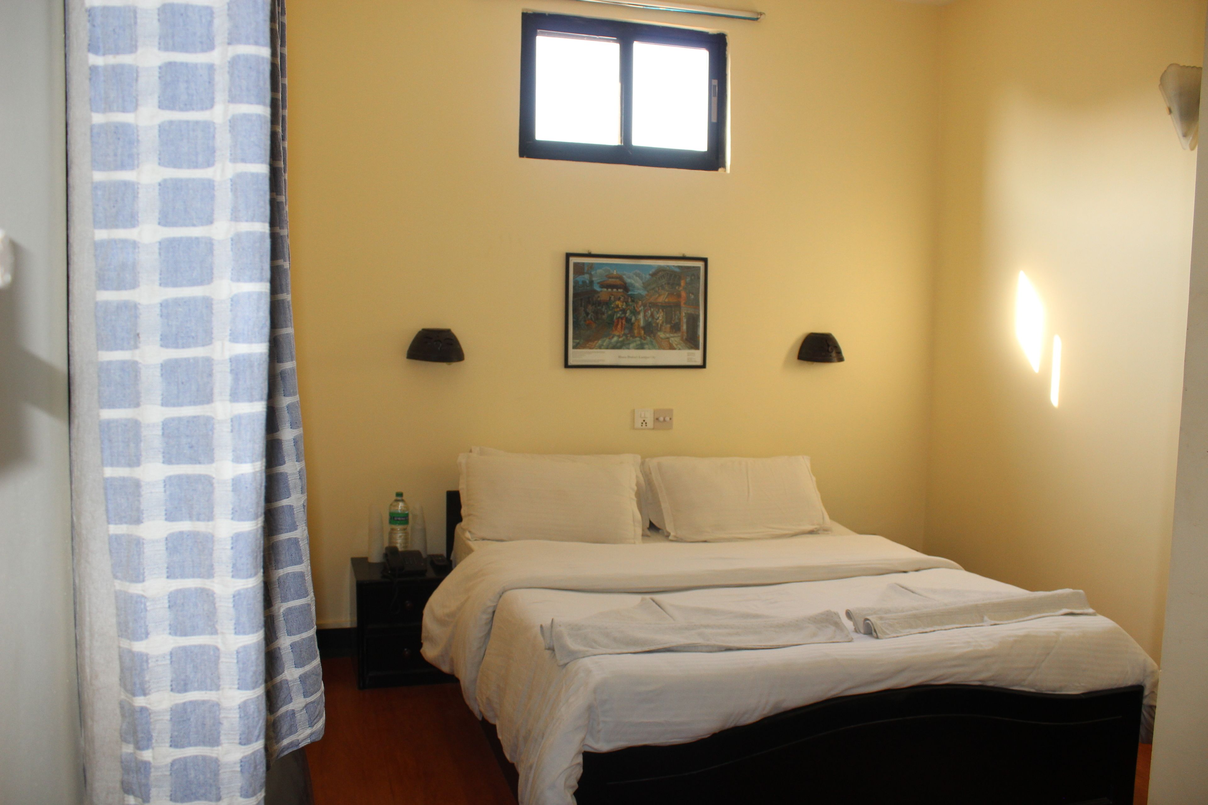 A bedroom with a bed, two bedside lamps, a nightstand, a painting on the wall, and a window.