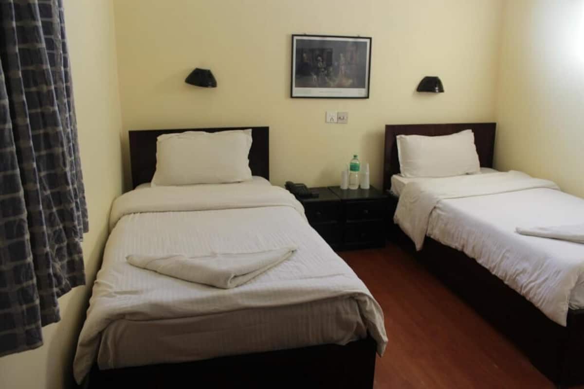 A hotel room with two beds, a nightstand, a framed picture on the wall, and a curtain.