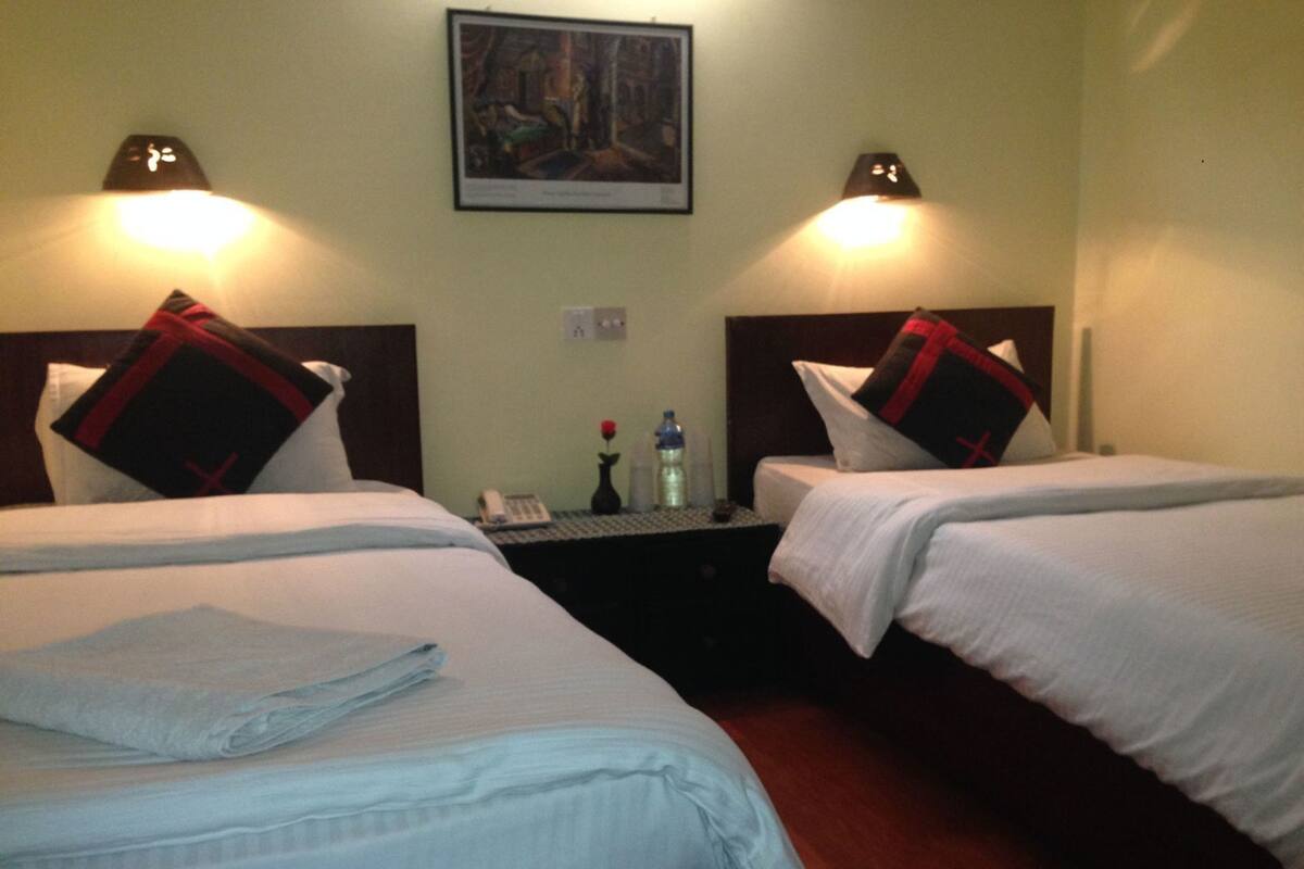 A hotel room with two beds, a nightstand, a painting on the wall, and two wall lamps.
