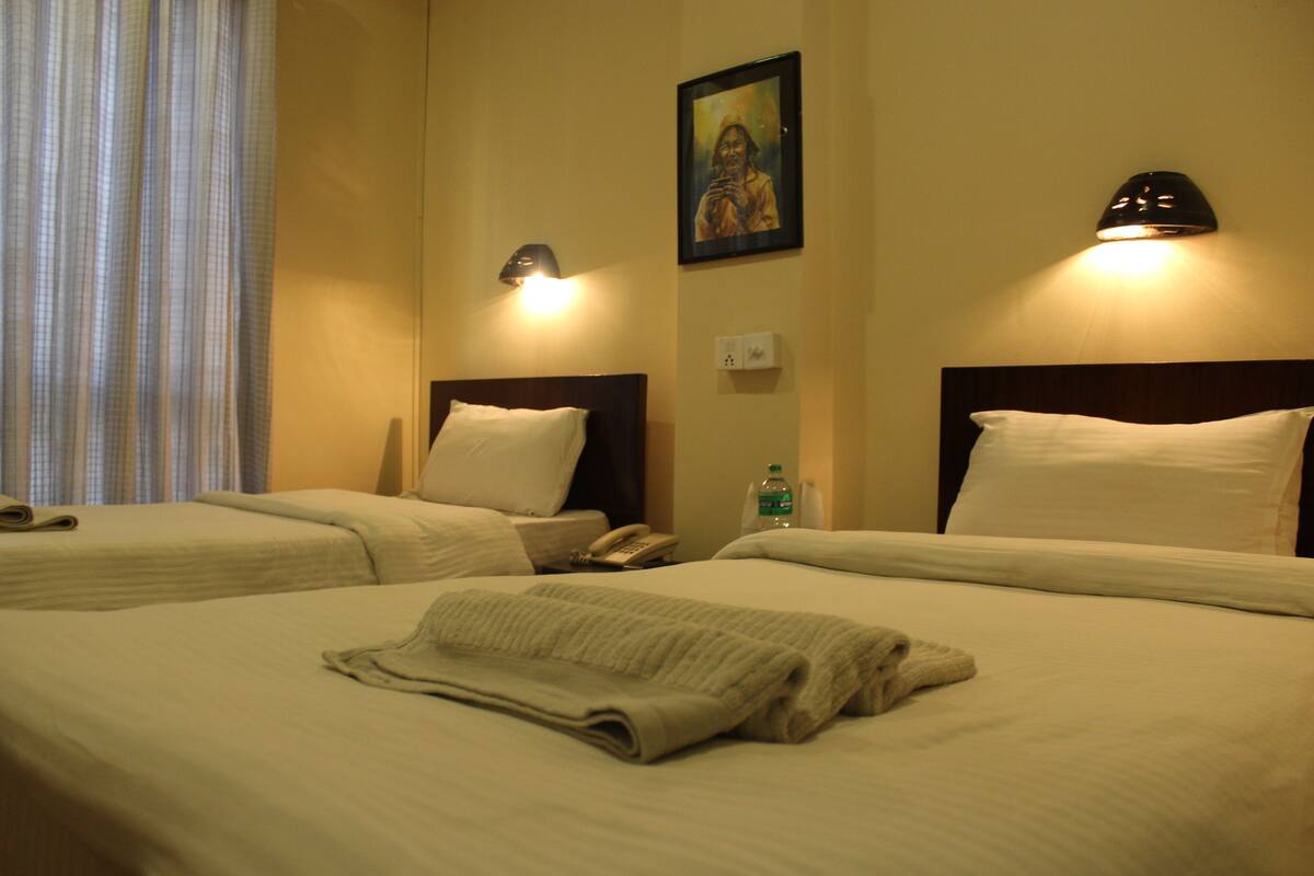 A hotel room with two beds, each with a headboard, a nightstand, a lamp, and a painting on the wall.