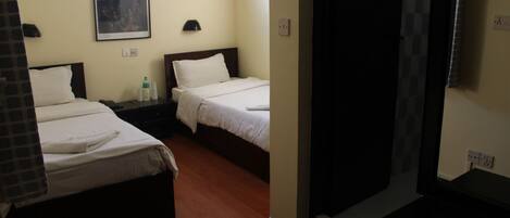 Habitación de hotel con dos camas individuales, una mesita de noche con lámpara, un cuadro en la pared y una ventana.