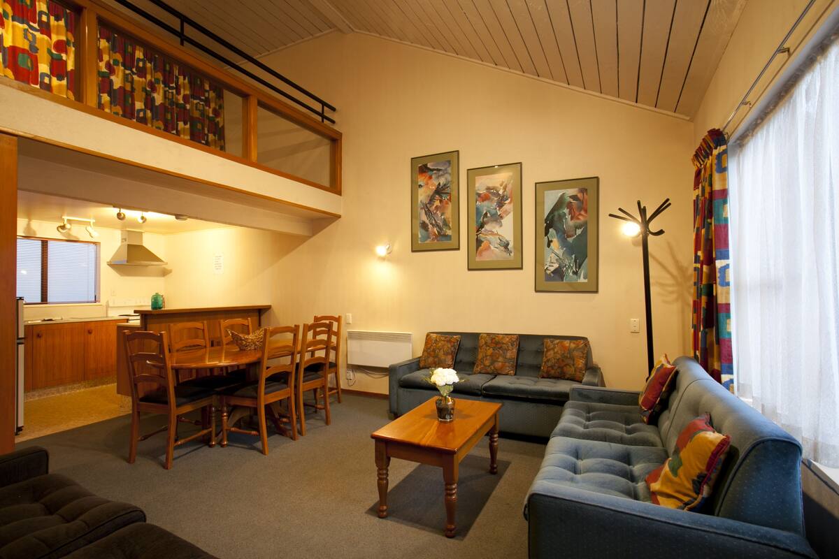 A living room with a dining area, a sofa, a coffee table, and a staircase leading to an upper level.