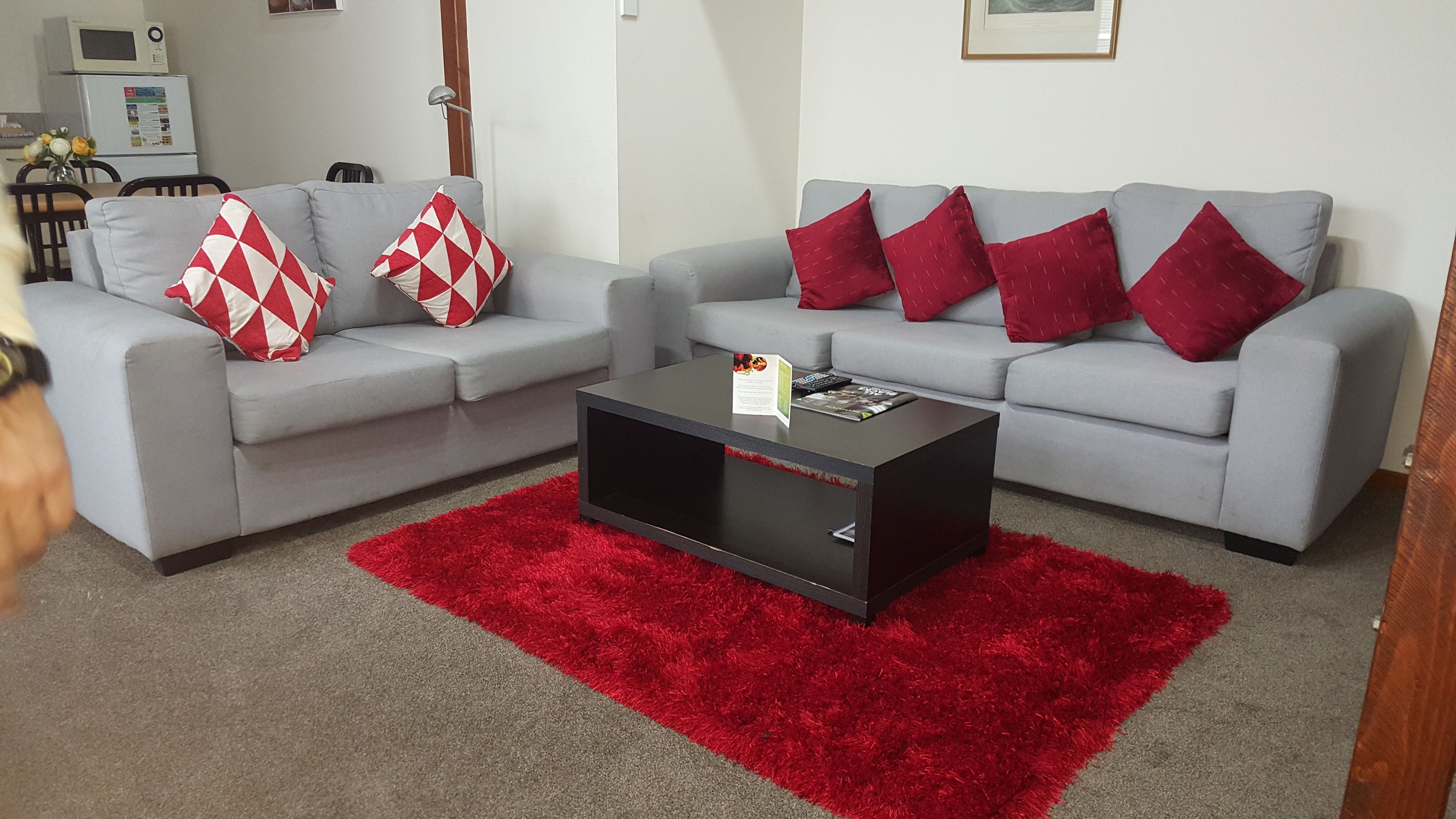 A living room with two grey sofas, red and white patterned cushions, a black coffee table, and a red shag rug.