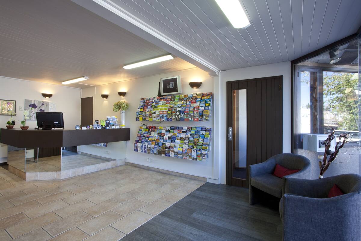 A reception area with a desk, chairs, a wall-mounted display of brochures, and a large window offering a view of the outdoors.