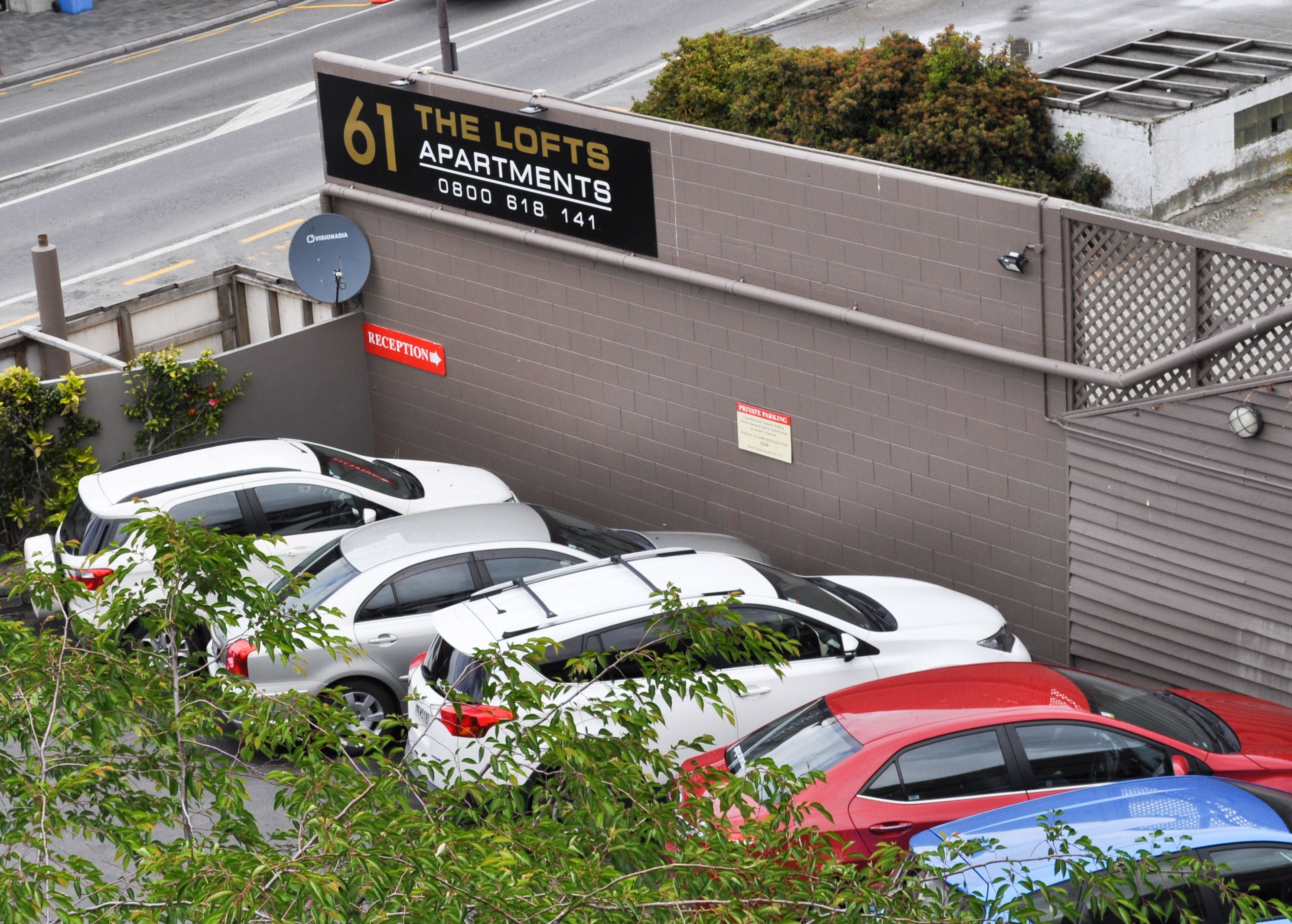 A parking area with multiple cars, a reception sign, and a building with a sign indicating '61 The Lofts Apartments'.