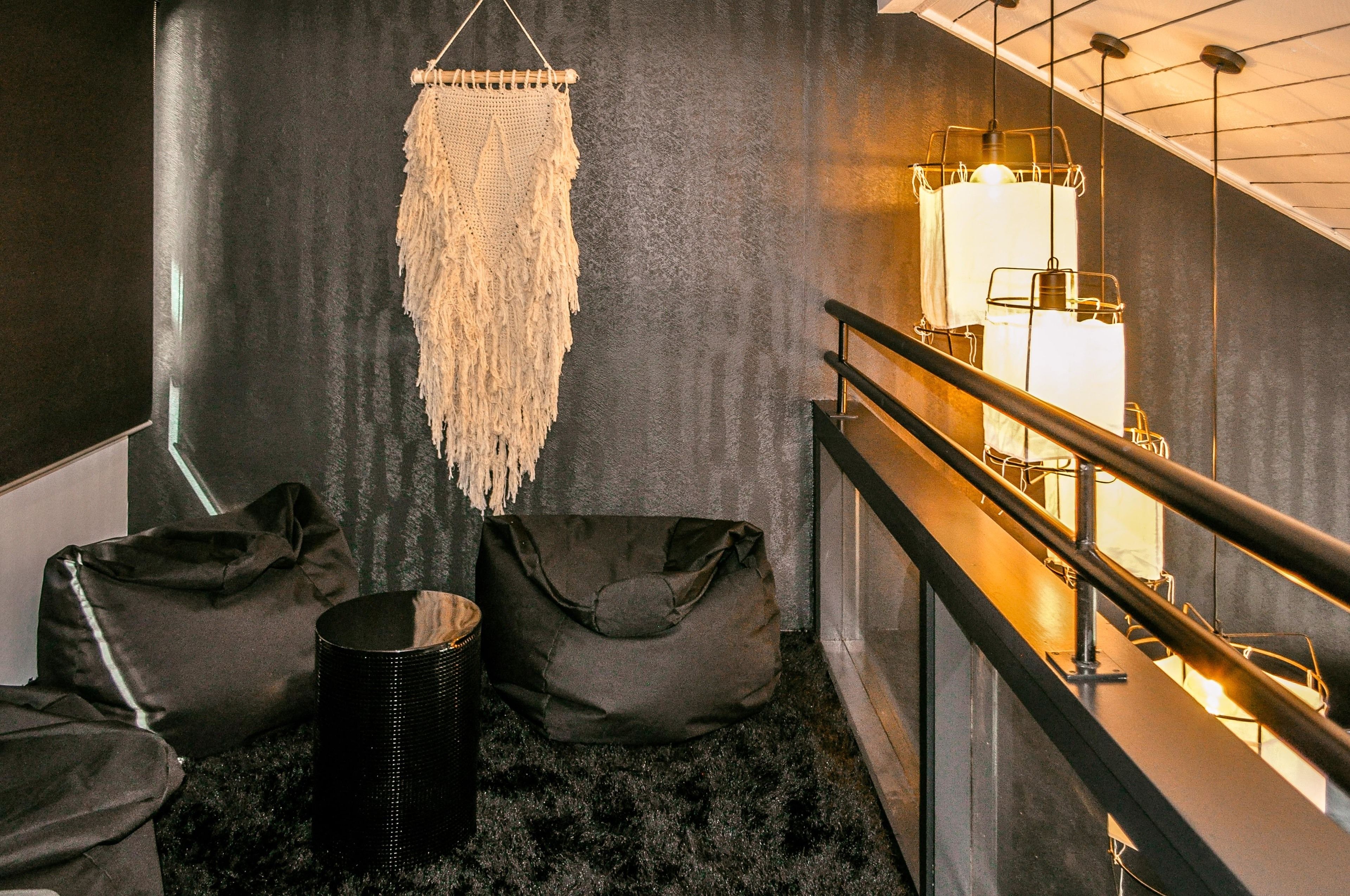 A modern interior with a macrame wall hanging, a black cylindrical object, and a seating area with a bench and a bag.