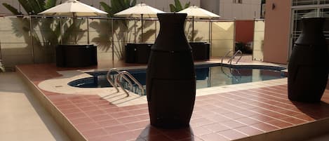 A swimming pool with tiled flooring, metal railings, and umbrellas.