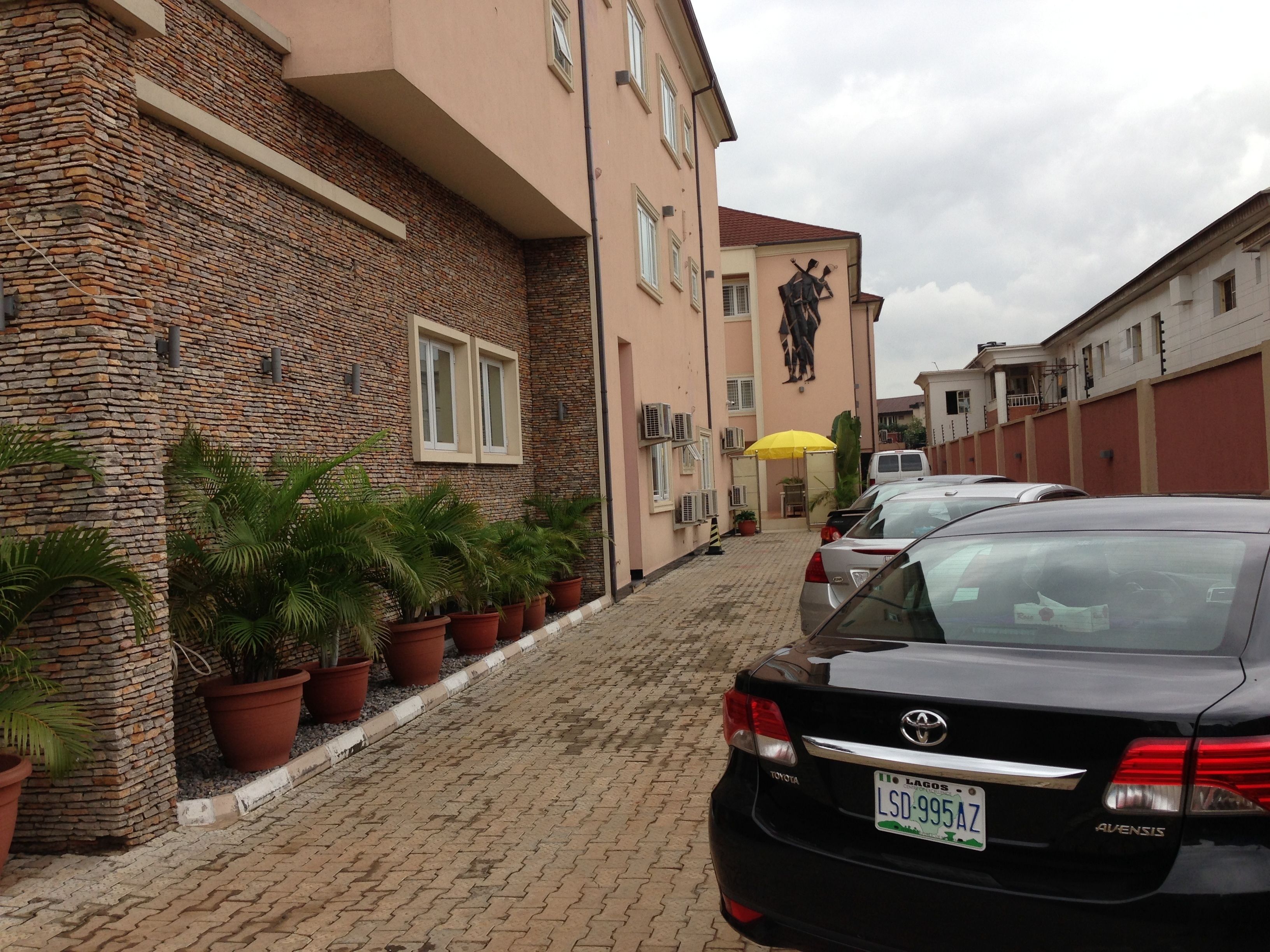 A black Toyota Avensis parked on a cobblestone street, with a building featuring a stone facade and a statue on the wall.