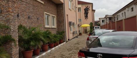 A black Toyota Avensis parked on a cobblestone street, with a building featuring a stone facade and a statue on the wall.