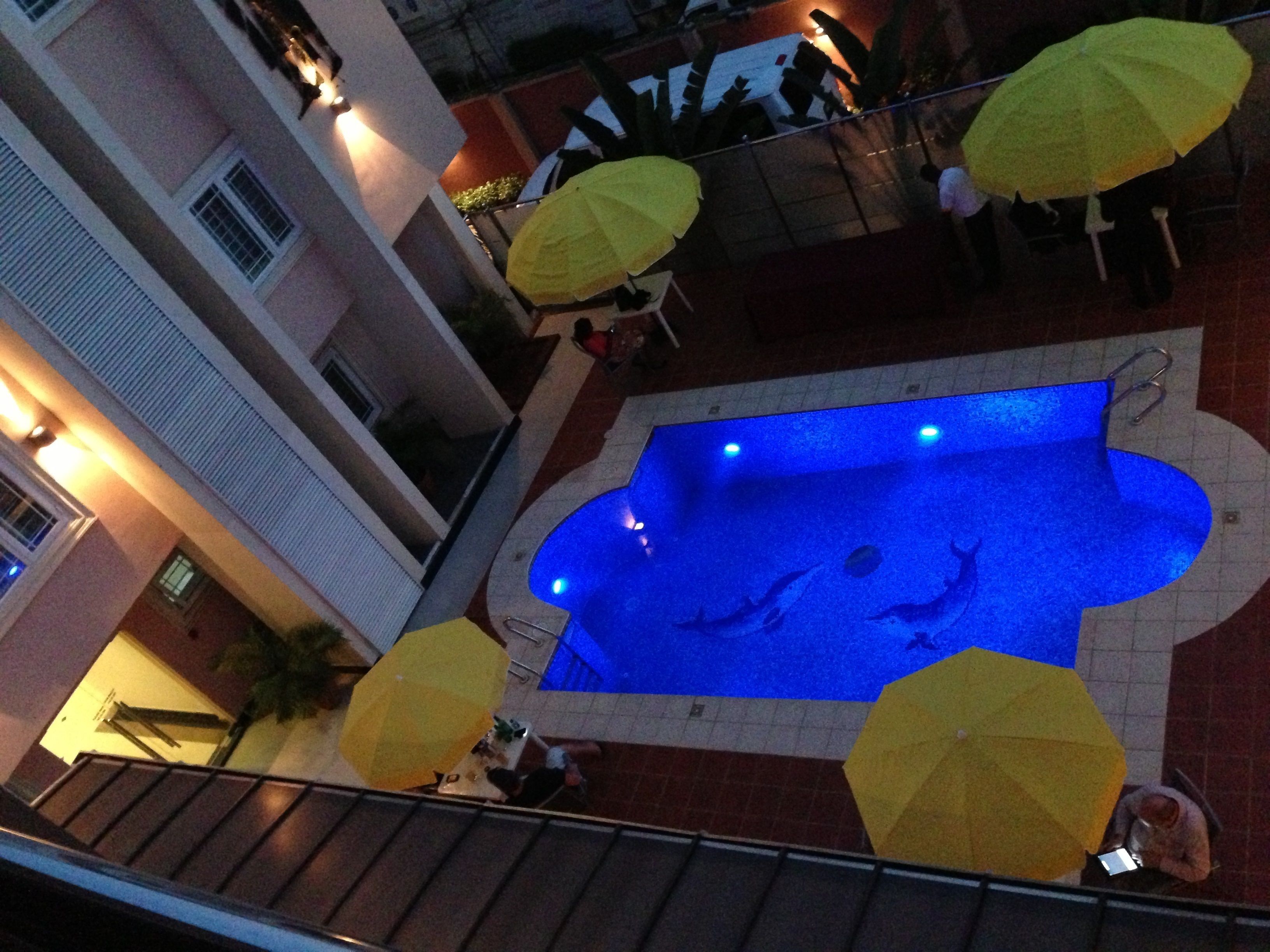 A swimming pool with a blue interior, surrounded by yellow umbrellas and a tiled floor.