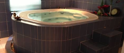 Un jacuzzi en esquina con calentador incorporado, un reloj y una pequeña planta en la pared.