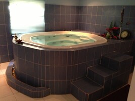 A corner jacuzzi with a built-in heater, a clock, and a small plant on the wall.