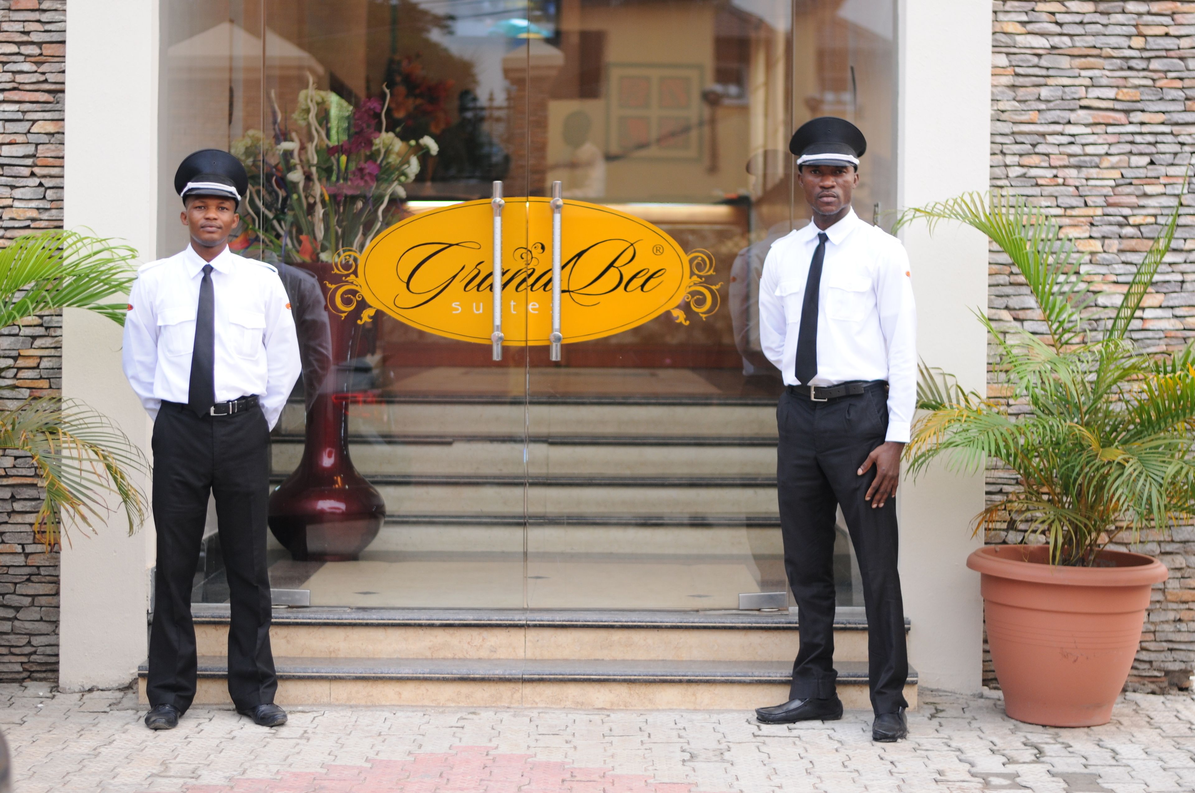 Two uniformed staff members standing in front of a hotel entrance with a sign that reads "Gracia Bee Suite".