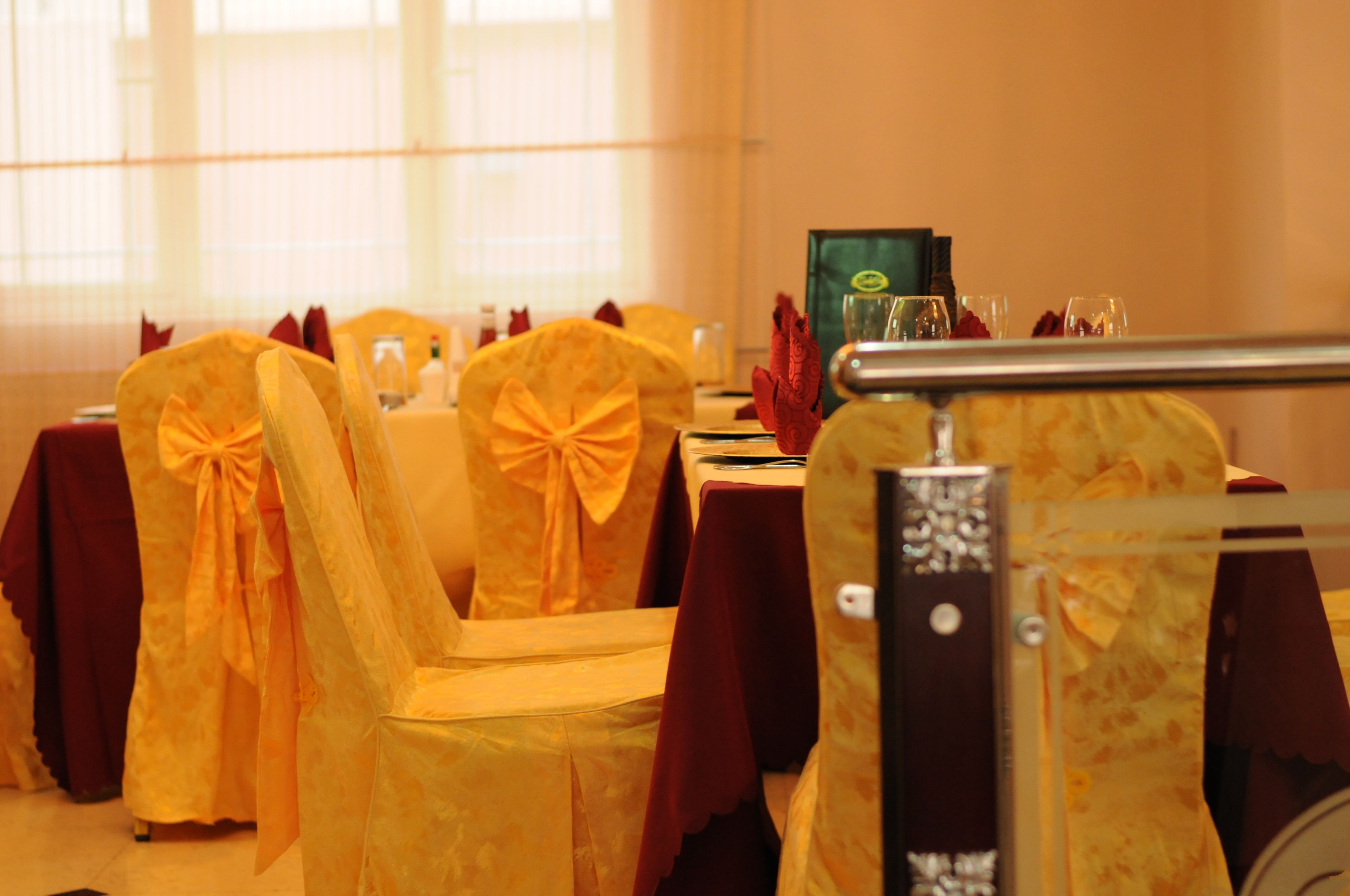 A dining area with tables set for a meal, chairs with yellow sashes, and a glass partition.
