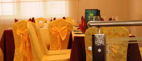 Un comedor con mesas dispuestas para una comida, sillas con cintas amarillas y un panel de vidrio.