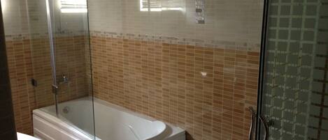 Un baño con bañera, cabina de ducha de vidrio y paredes de azulejos.