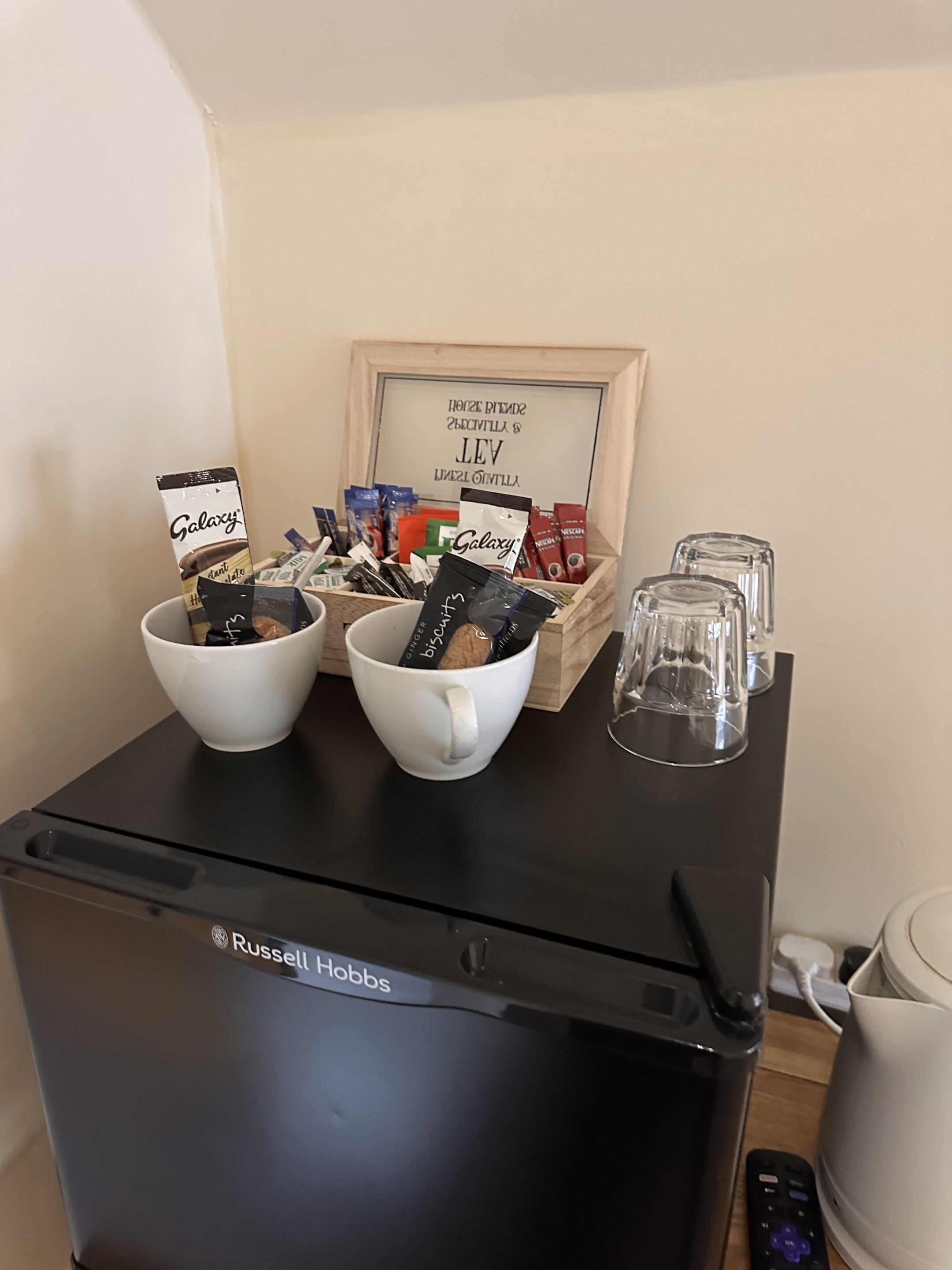 Een keukenhoek met een koelkast, twee witte kommen met chocoladerepen, een schaal met diverse snacks en een lijst in een lijst.