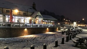 A snow-covered waterfront area with a building featuring large windows and a covered walkway. - Half Moon Jackfield (Telford)