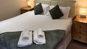 A neatly made bed with white linens, two pillows, a green blanket, and two folded towels. There is a modern abstract painting on the wall above the bed. - Half Moon Jackfield (Telford)
