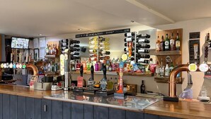 A bar with a variety of liquor bottles, a selection of taps, and a digital screen displaying content. - Half Moon Jackfield (Telford)