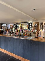 Um bar com diversas garrafas de bebidas, uma seleção de torneiras e uma tela digital exibindo conteúdo.