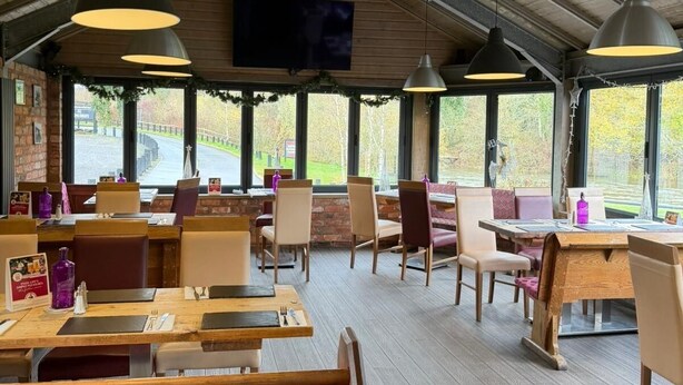 A restaurant with wooden tables and chairs, large windows, and hanging pendant lights. - Half Moon Jackfield (Telford)