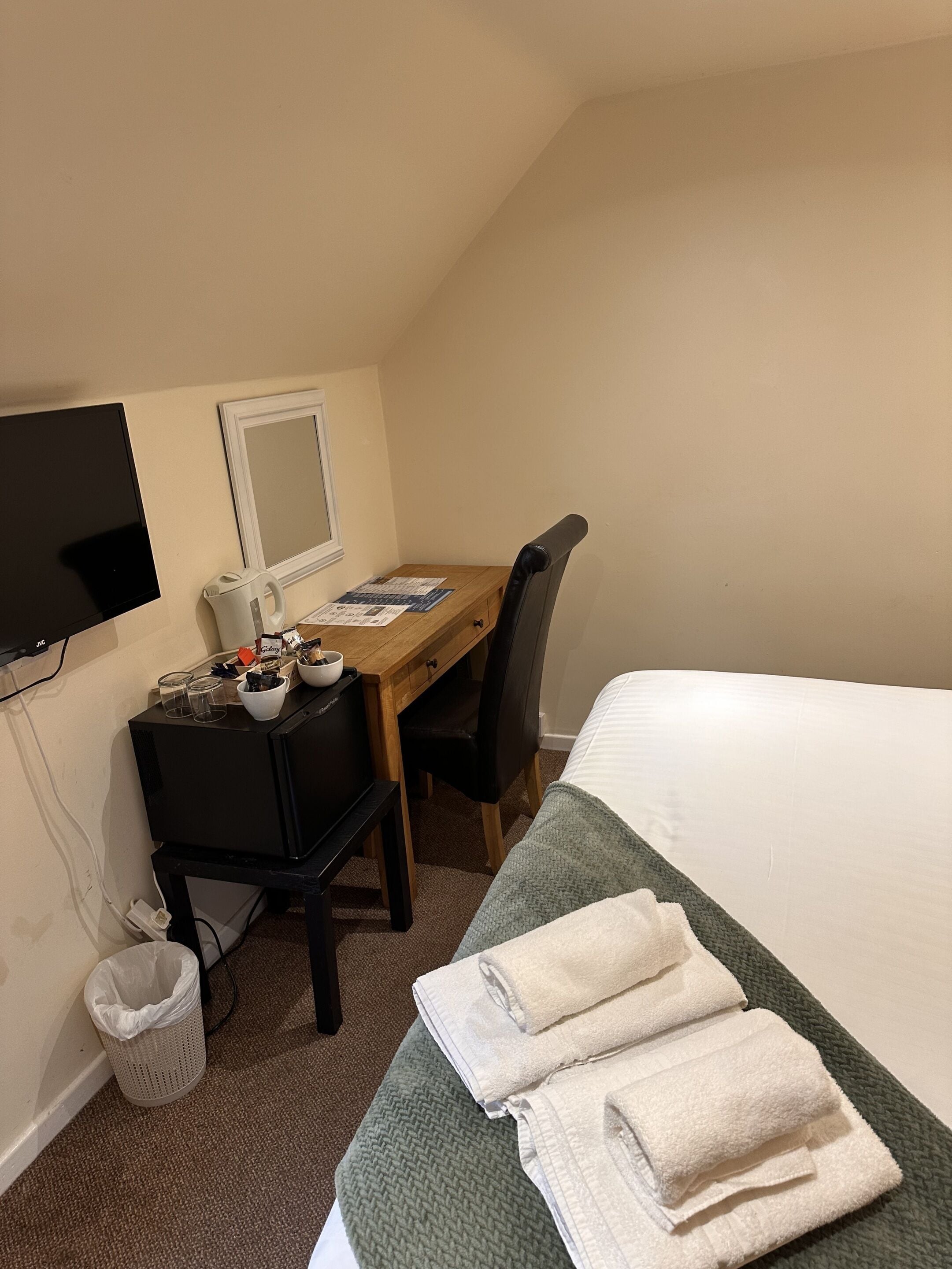Et hotelværelse med en seng, et skrivebord med computer, en stol, et fjernsyn og et vindue.