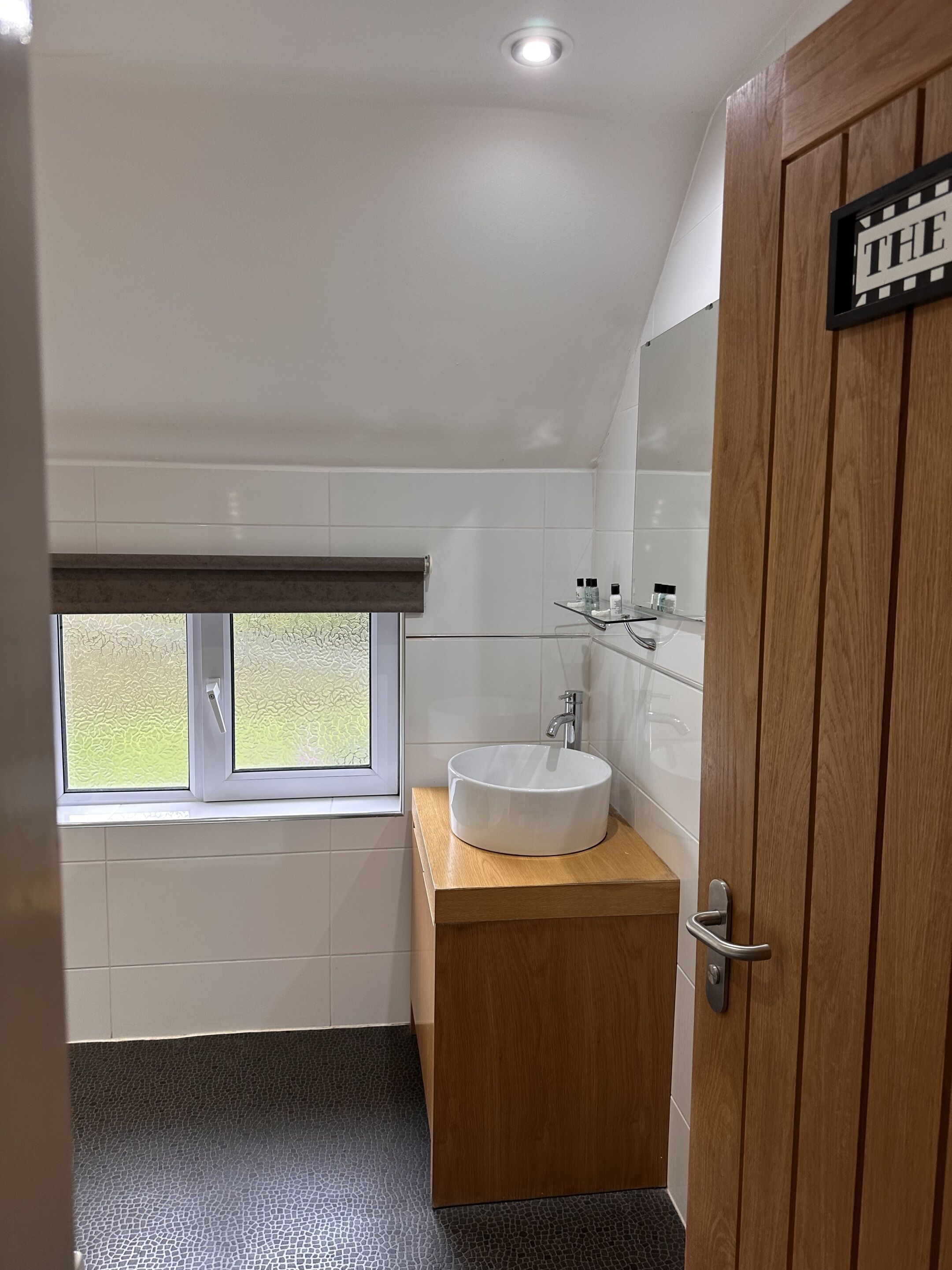 A bathroom with a white sink, wooden vanity, and a window with frosted glass.
