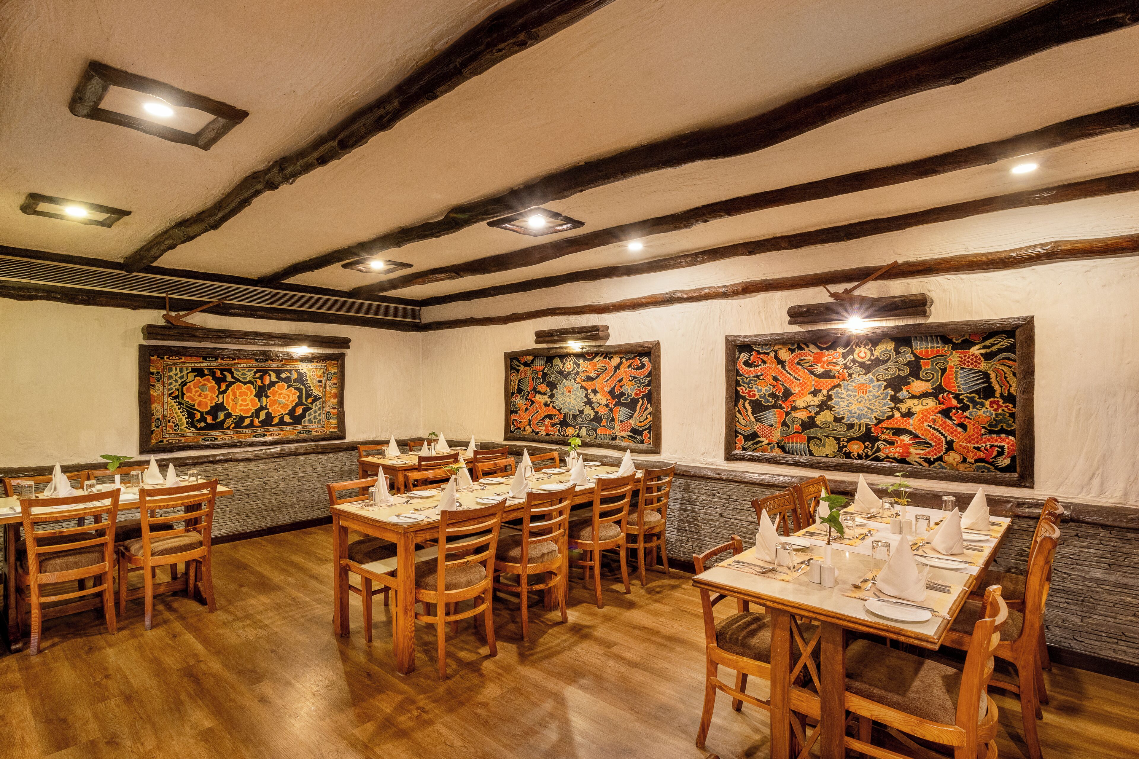 Un restaurante con mesas y sillas de madera, paredes de piedra y arte tradicional.