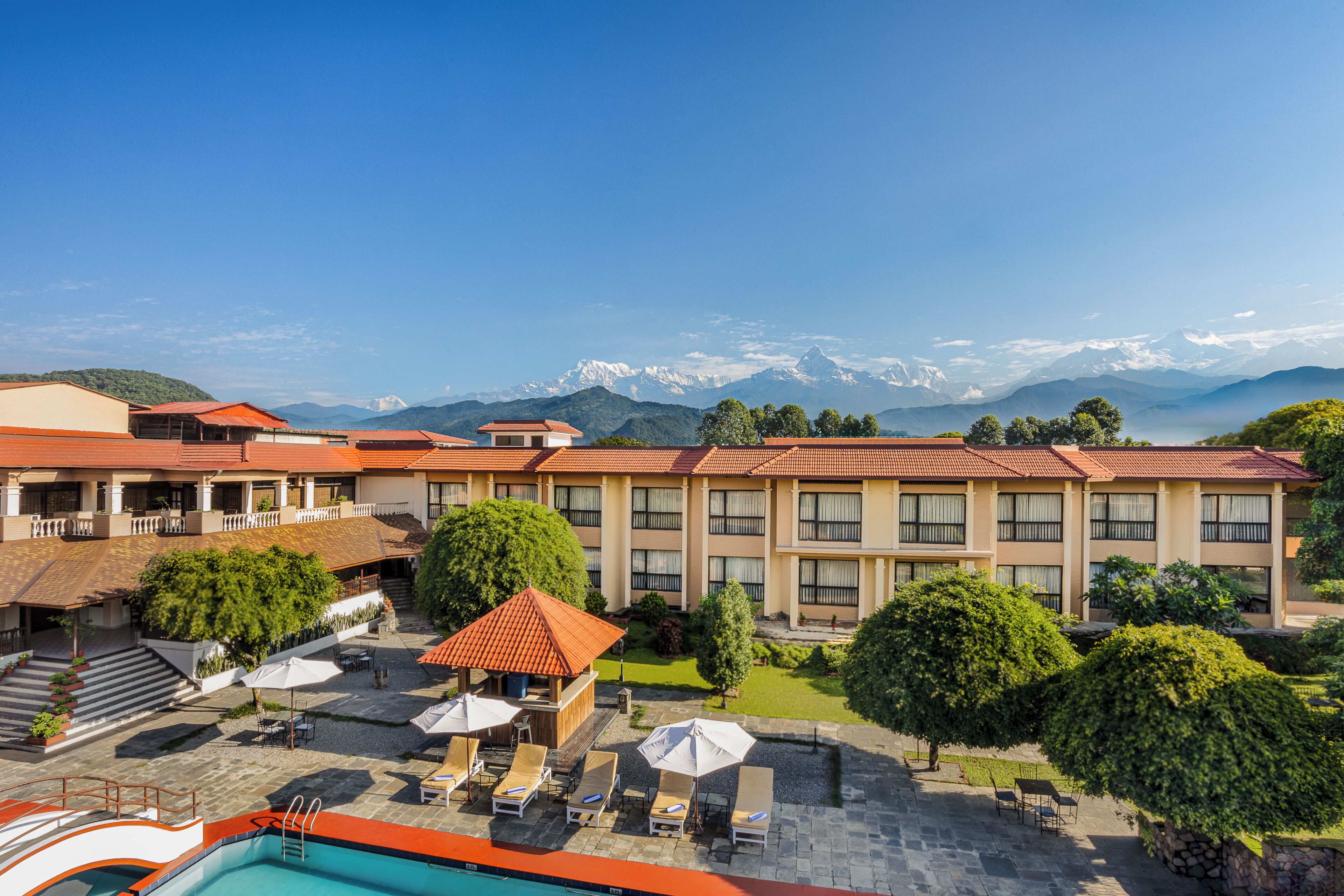 Un hotel con piscina, area salotto esterna e vista sulle montagne innevate.