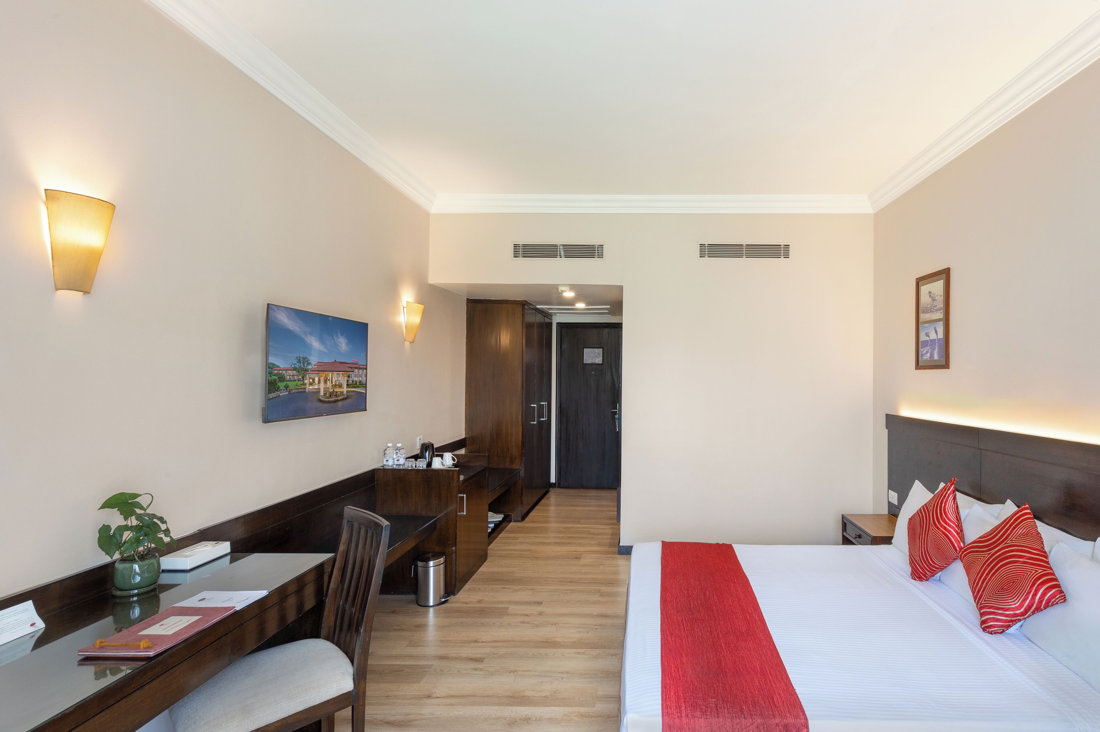 Una habitación de hotel con cama, escritorio, silla, una mesita, un cesto de basura y un cuadro en la pared.