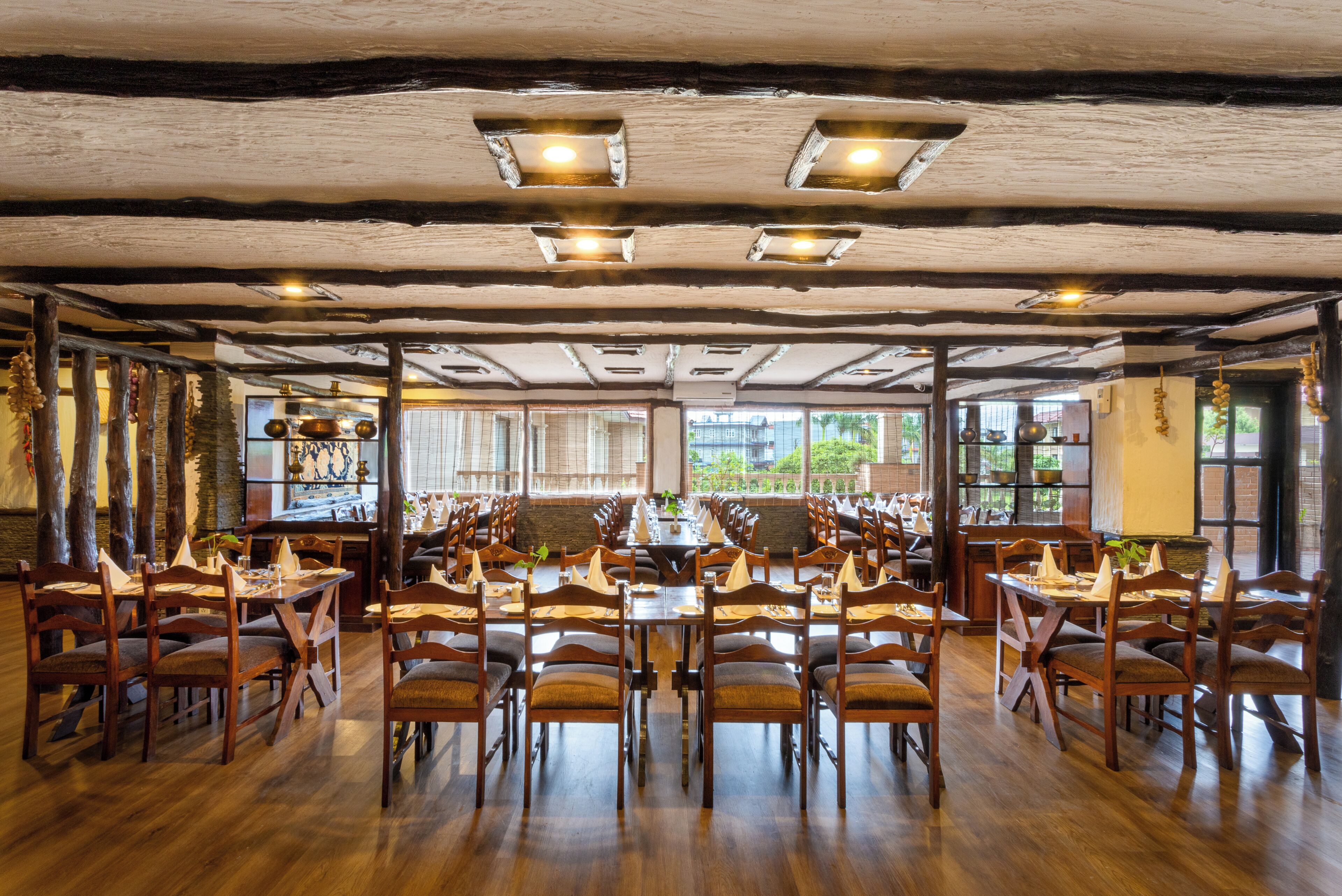 Un restaurante con mesas y sillas de madera, amplios ventanales y un techo rústico.