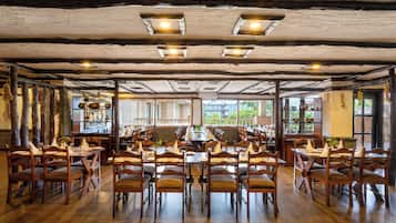 Un restaurante con mesas y sillas de madera, amplios ventanales y un techo rústico.