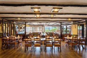 Un restaurante con mesas y sillas de madera, amplios ventanales y un techo rústico.