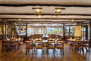 Un restaurante con mesas y sillas de madera, amplios ventanales y un techo rústico.